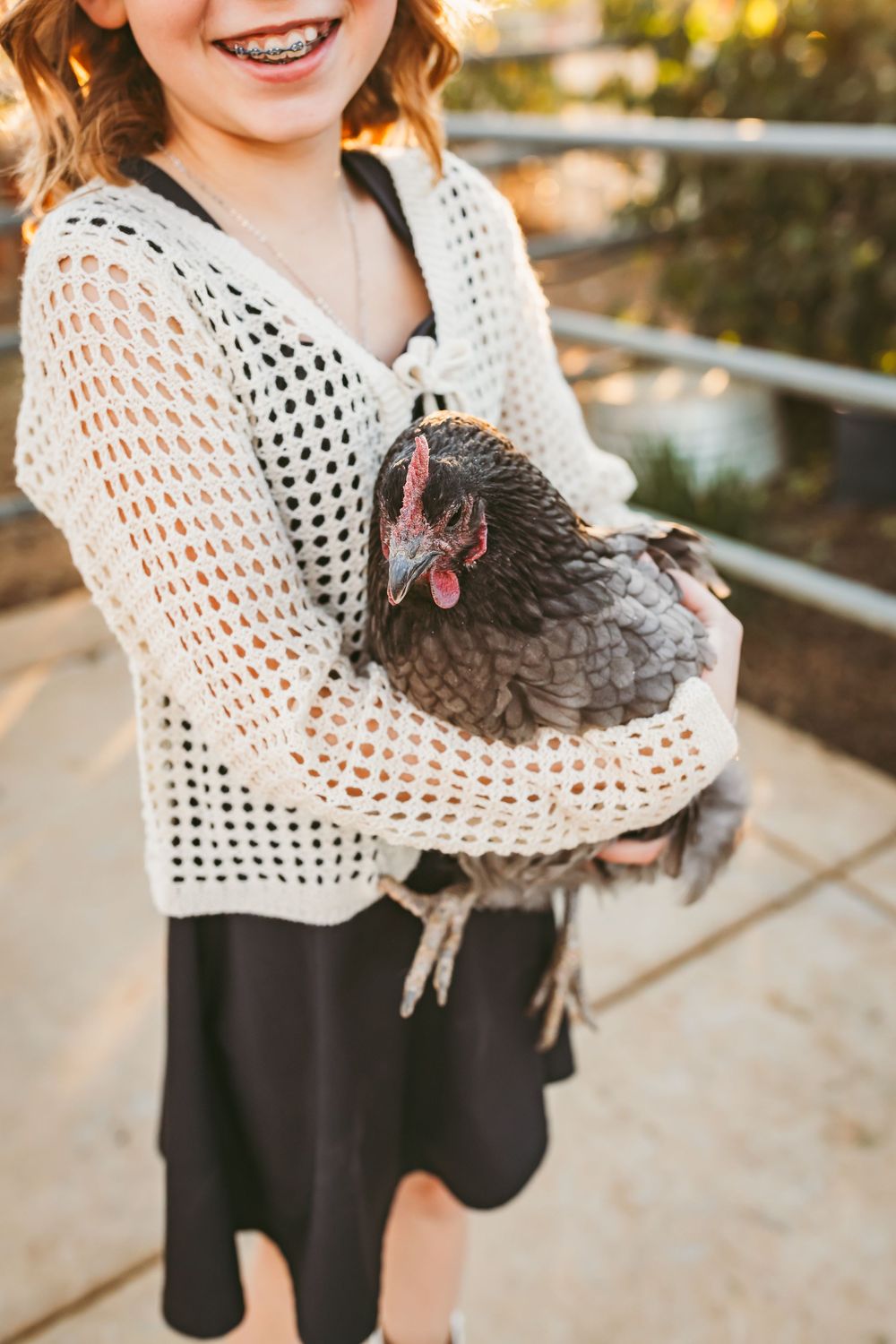 Person wearing a white crochet sweater holds a fluffy chicken in their arms.