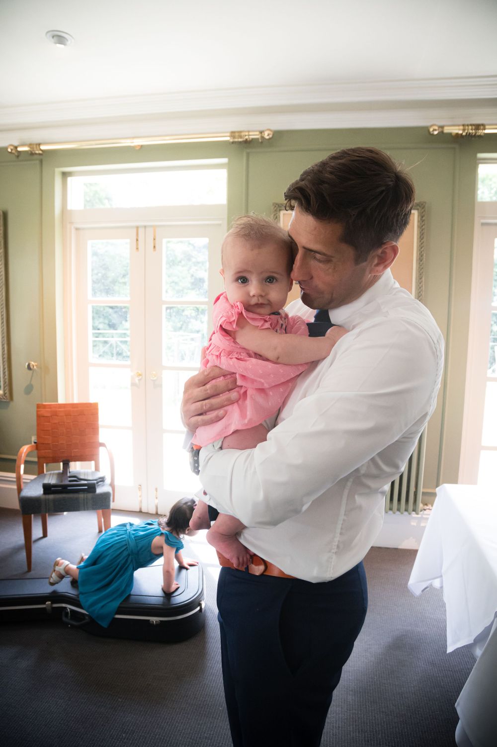 A tender moment between a parent and baby wearing pink in a sunlit room with dark wood floors and light green walls.