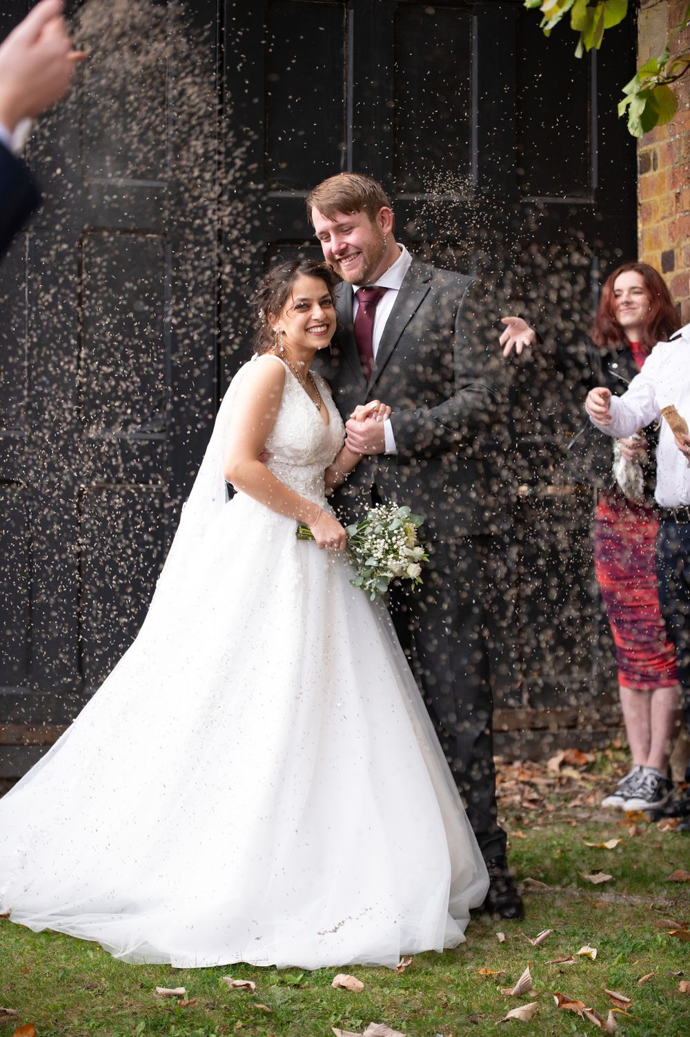 A joyful couple celebrates their wedding day outdoors while guests throw confetti in a beautiful garden setting.