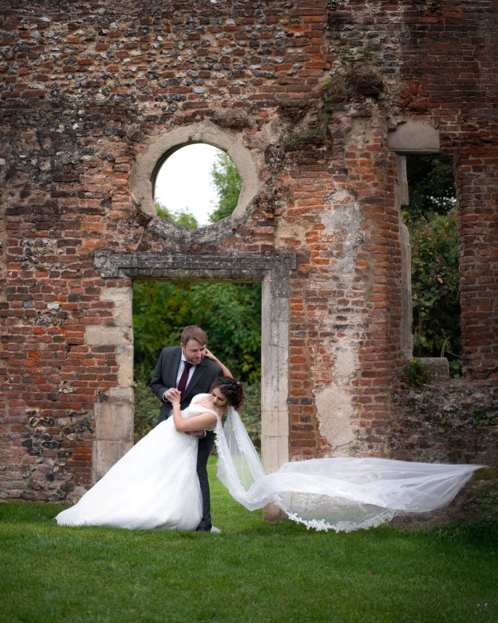 A romantic wedding photo series showing a couple posing against weathered brick ruins in a garden setting.