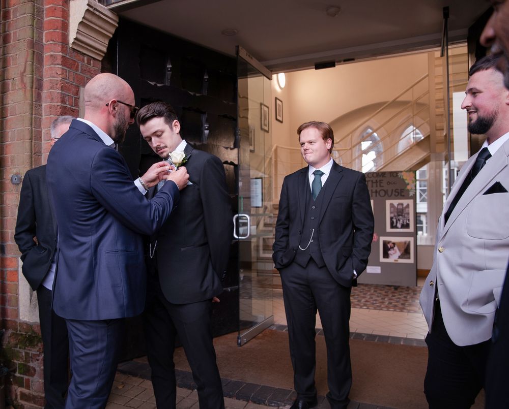 A group of men in formal suits gather in a hallway, having a conversation near a curved archway entrance.