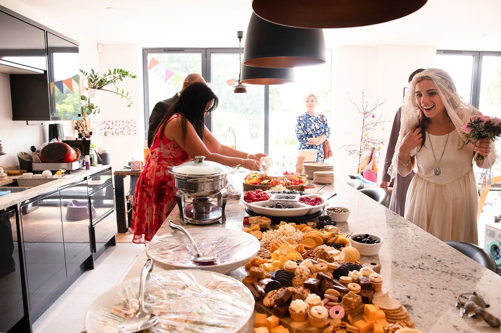 People gathering around a buffet table with pastries and treats at a wedding reception in a modern kitchen setting.