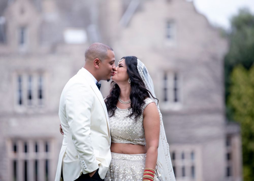 A couple in wedding attire share an intimate moment in front of a grand stone building.