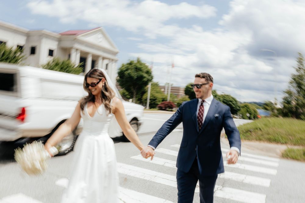 A couple in wedding attire holds hands and walks together on a sunny day.