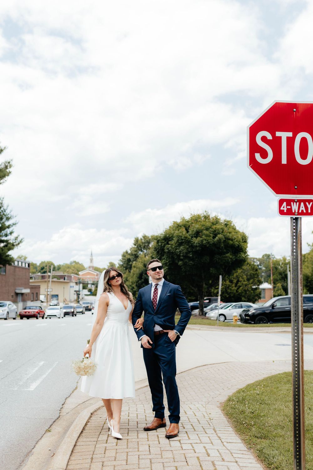 A couple poses playfully by a stop sign during their wedding photoshoot on a sunny day.