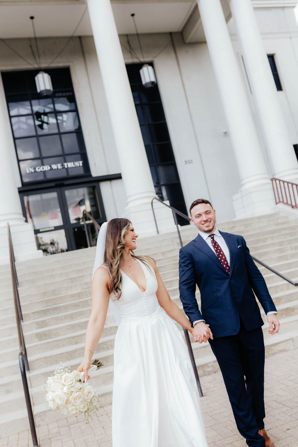 A couple shares a romantic moment on the steps of a white columned building during their wedding.