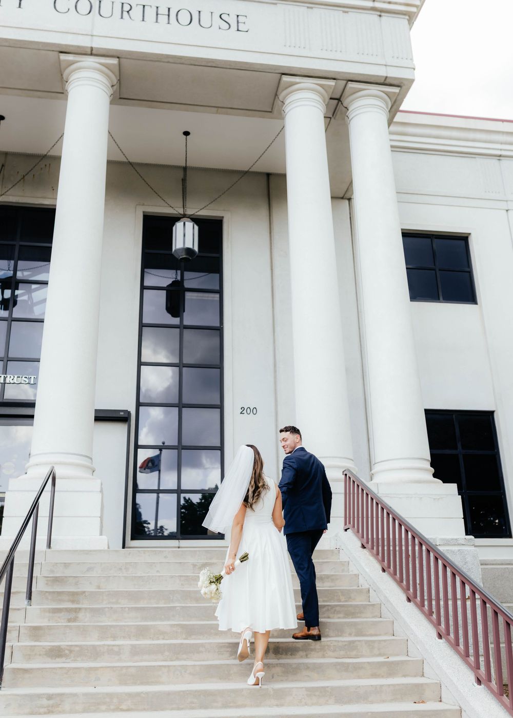 A panoramic view of a white courthouse building with couples standing on the steps for wedding photos.