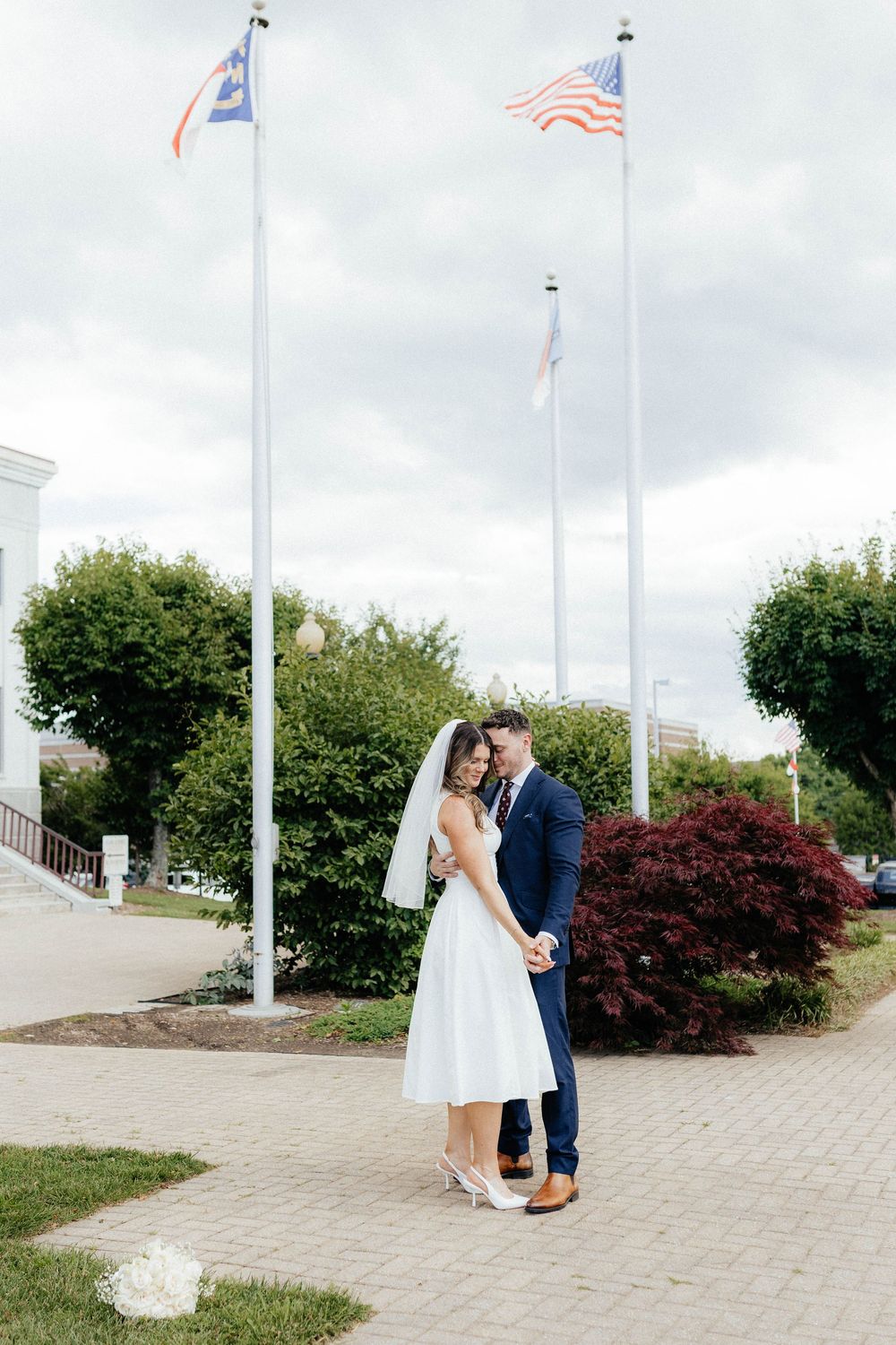 A newlywed couple poses beneath American flags during an outdoor wedding photoshoot.