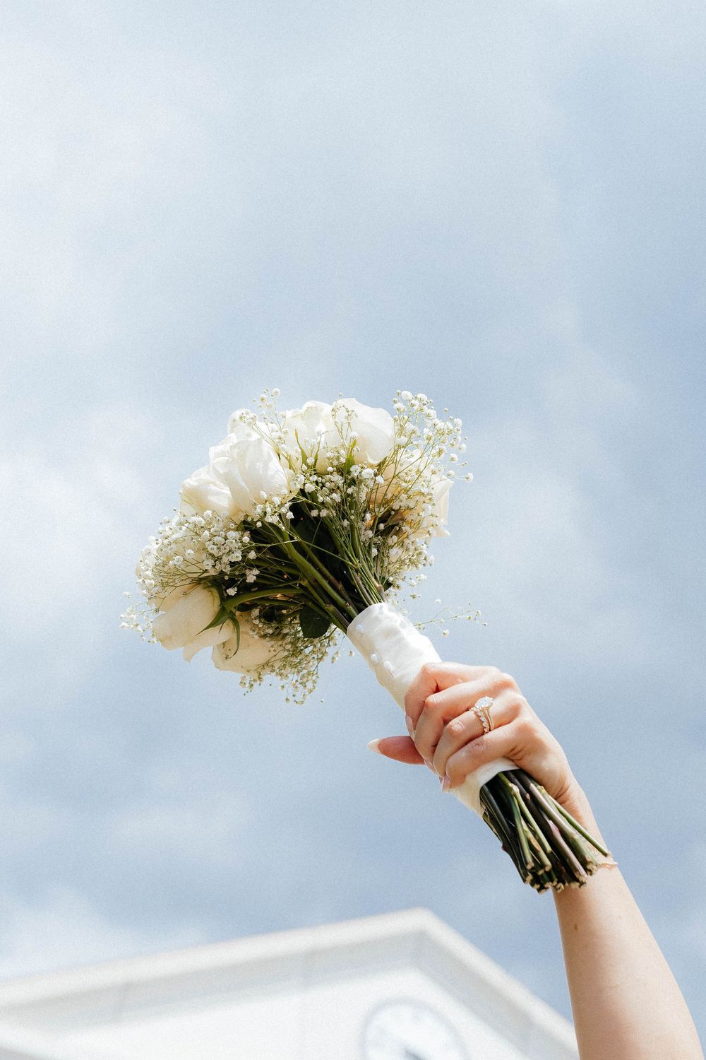 White floral bouquet held up against a cloudy sky with delicate baby's breath flowers.