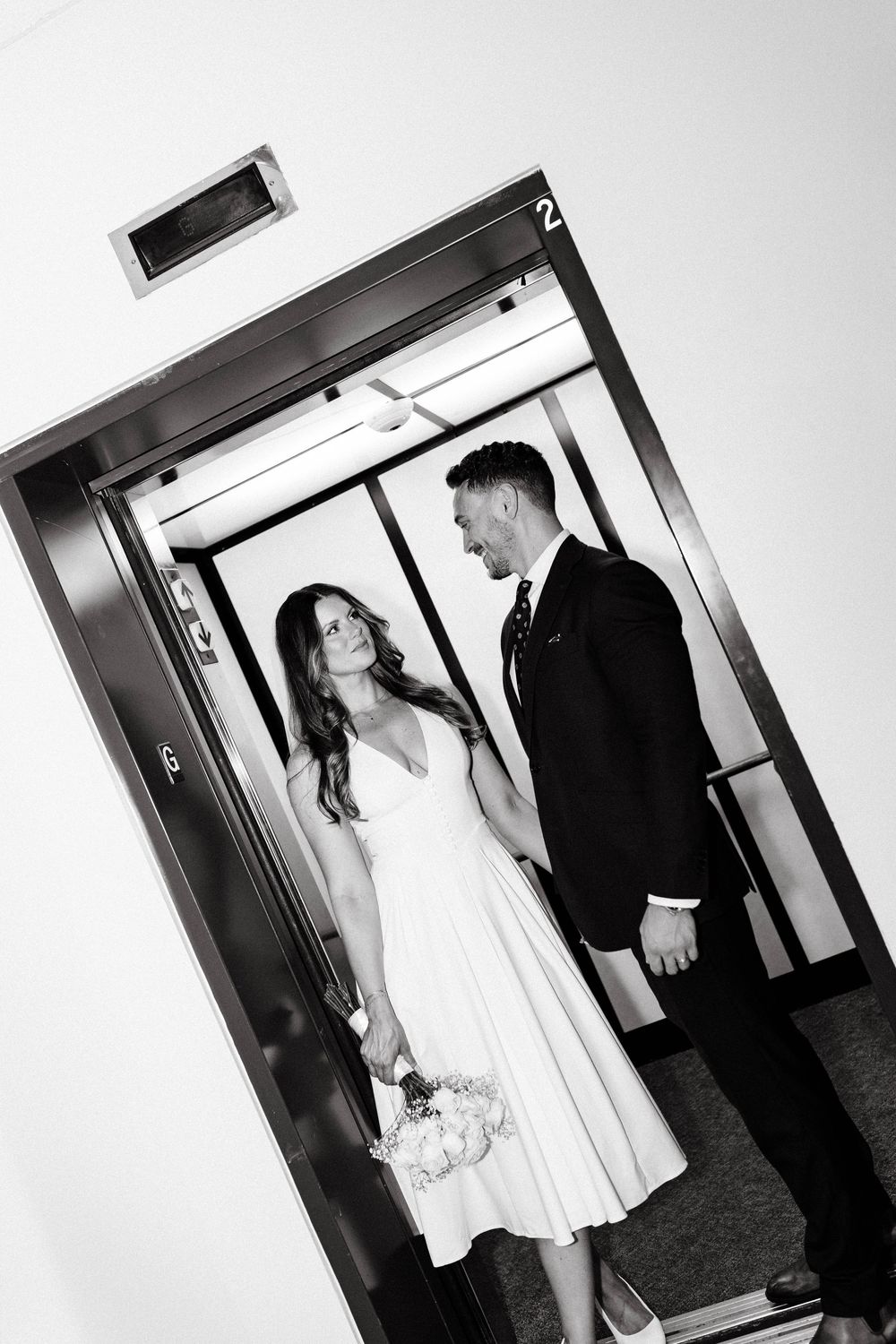 A black and white photo of a couple in formal attire standing in an elevator doorway.