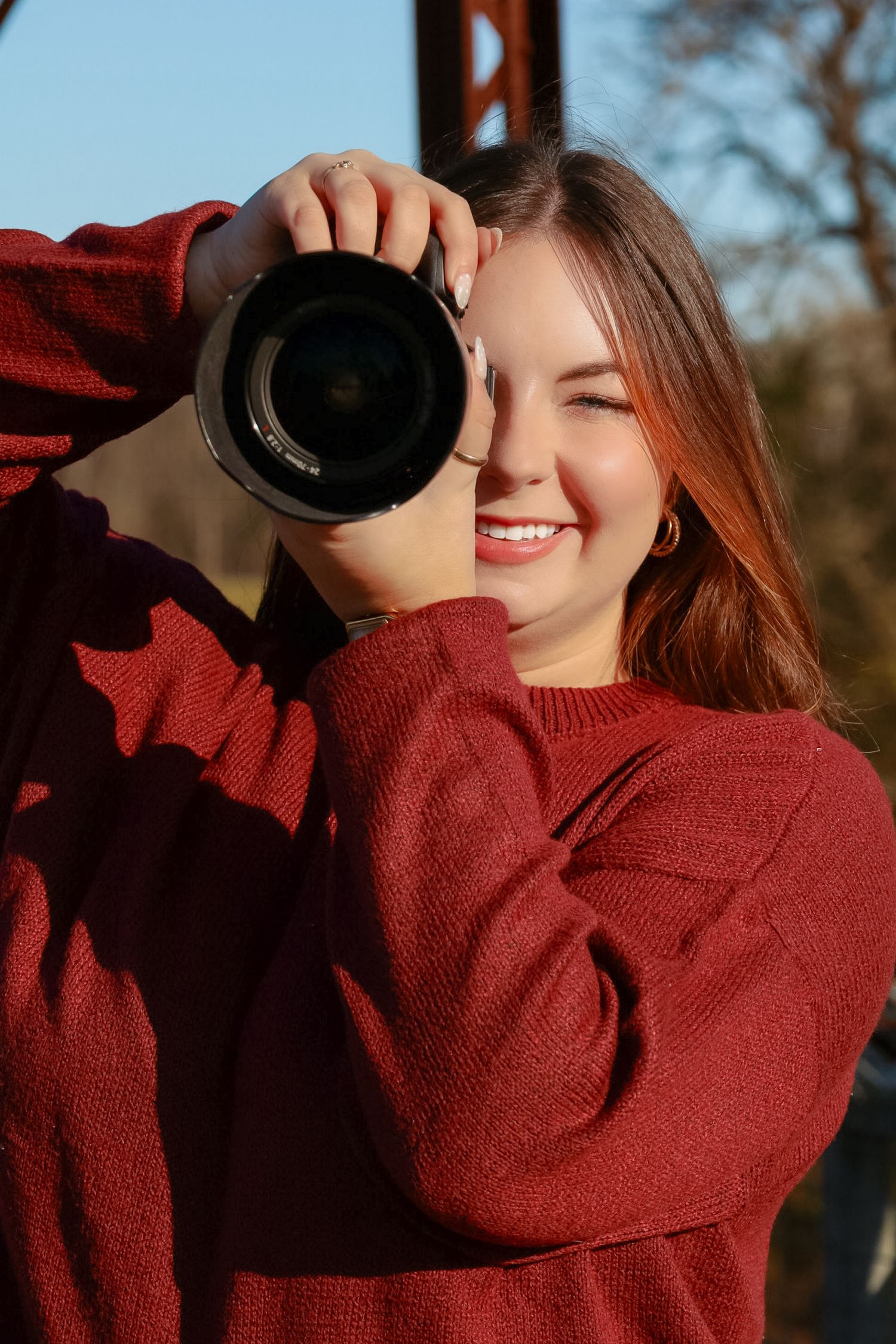 Photographer in burgundy sweater taking pictures outdoors at sunset.