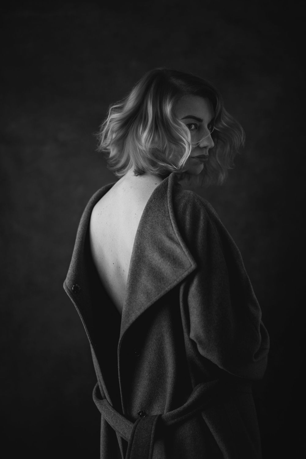 A dramatic black and white fashion photograph showing the exposed back of a dress against a dark background.