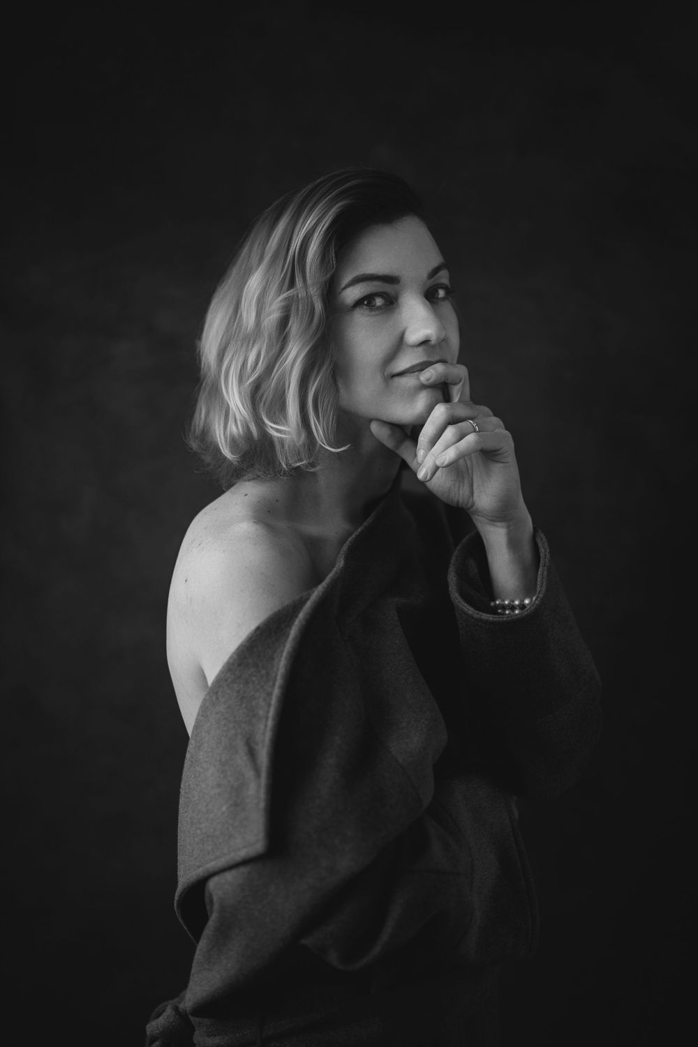 Black and white portrait of a person in an off-shoulder sweater with a contemplative expression against dark background.