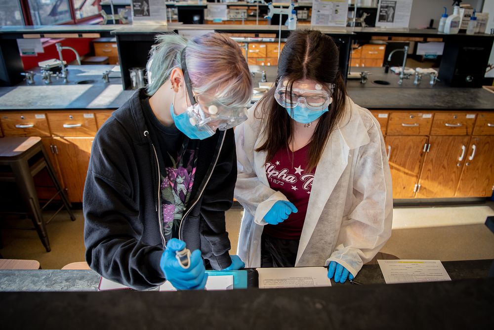 People in protective gear conducting laboratory experiments with scientific equipment.