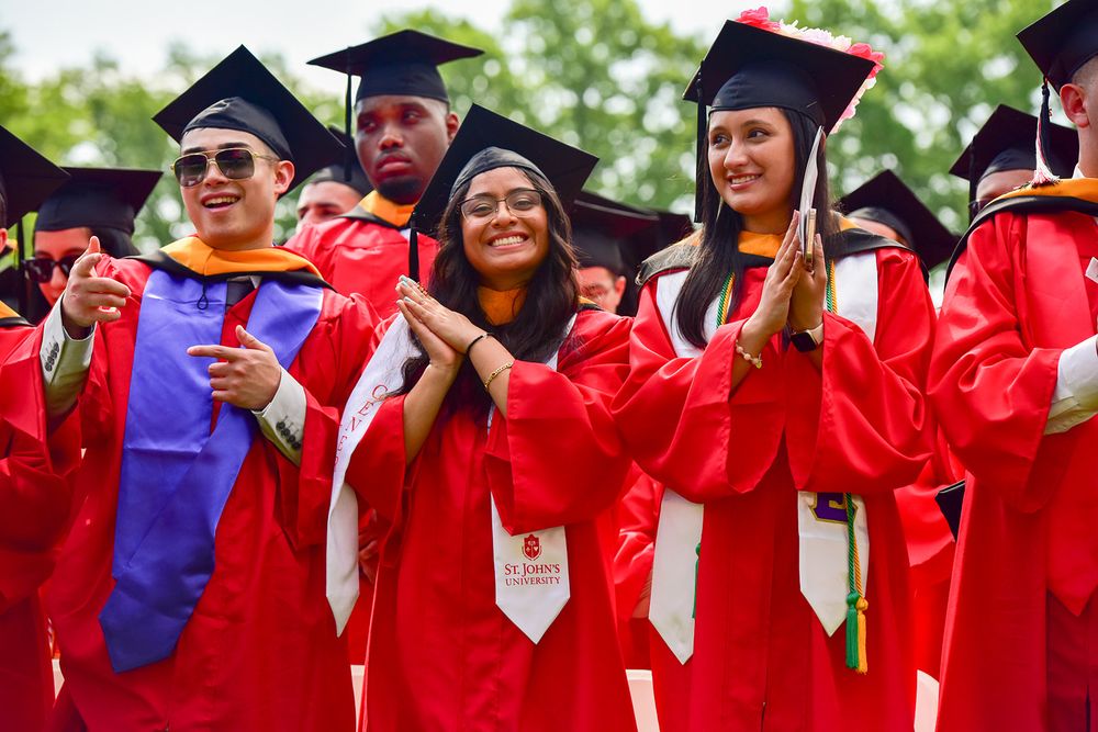 Graduates in bright red academic regalia and mortarboard caps celebrate during a commencement ceremony.