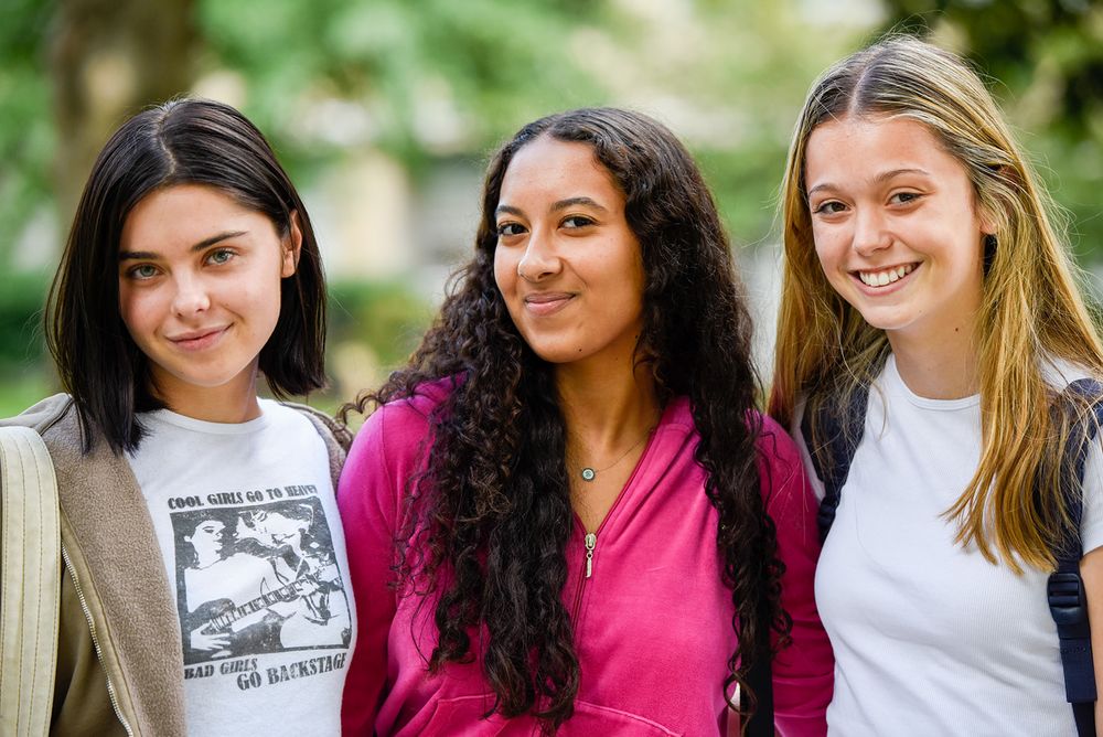A group of students smile together outdoors in a casual photo lineup against a green natural background.