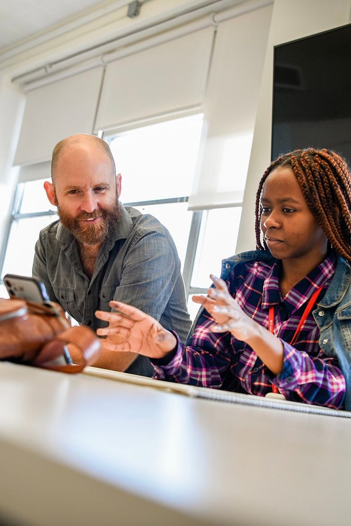 Two people engaged in conversation while sitting at a table in a bright office setting.