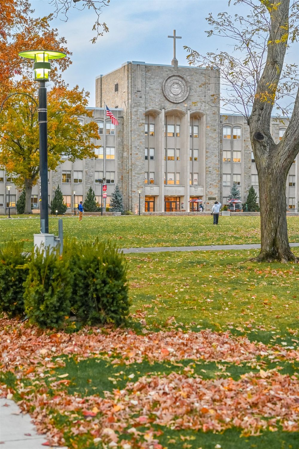 Stone church building on college campus with autumn leaves scattered across green lawn in foreground.