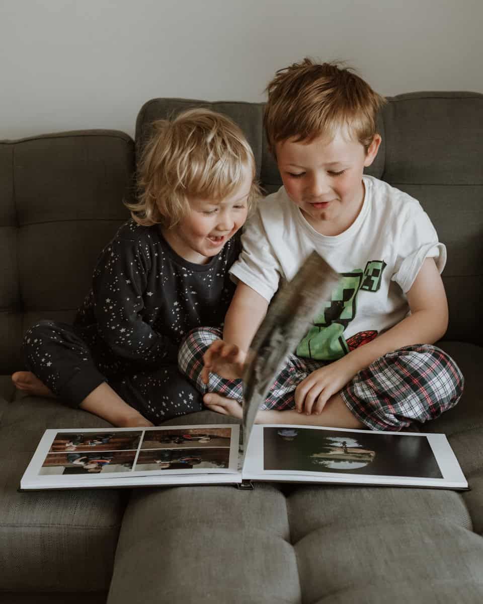 Two boys smile and laugh as they flip through the pages of their family photobook at home in Marlow.