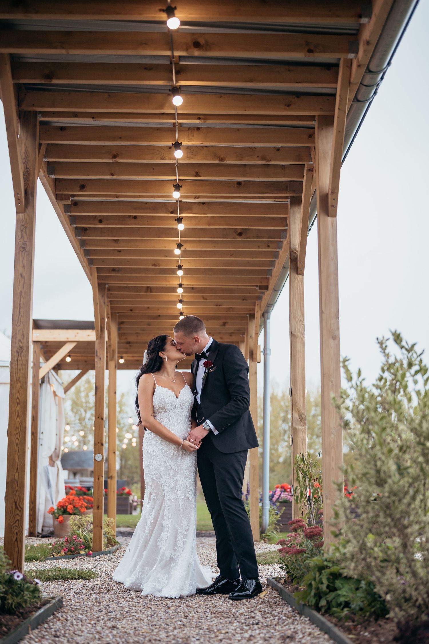 A couple shares a romantic moment under a covered walkway with string lights at an outdoor venue.