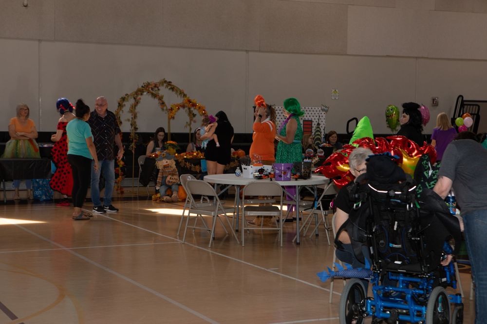 Indoor community event with tables and chairs set up in a gymnasium with festive decorations and attendees gathered.