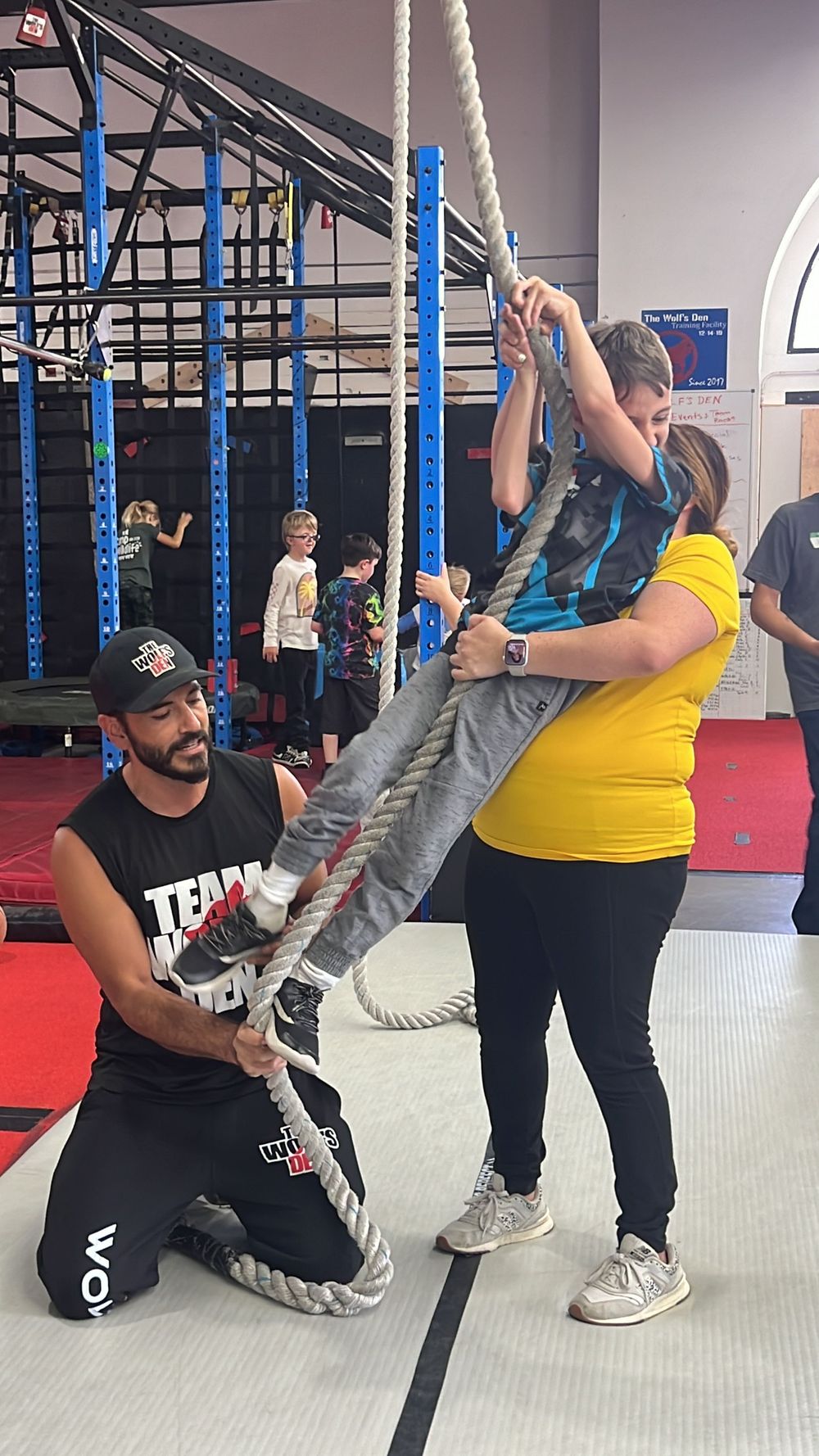 A sequence of photos showing a trainer demonstrating proper rope climbing technique in a gym setting.