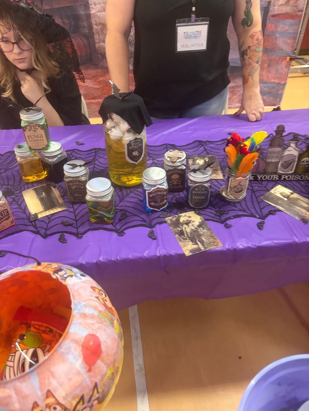 Mason jars and decorative items arranged on a purple tablecloth at what appears to be a craft fair or market display.