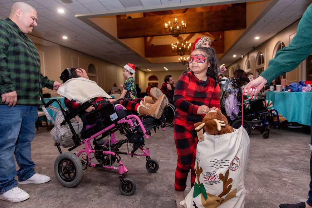 A group of people gather in a room with strollers and wheelchairs during an indoor event.