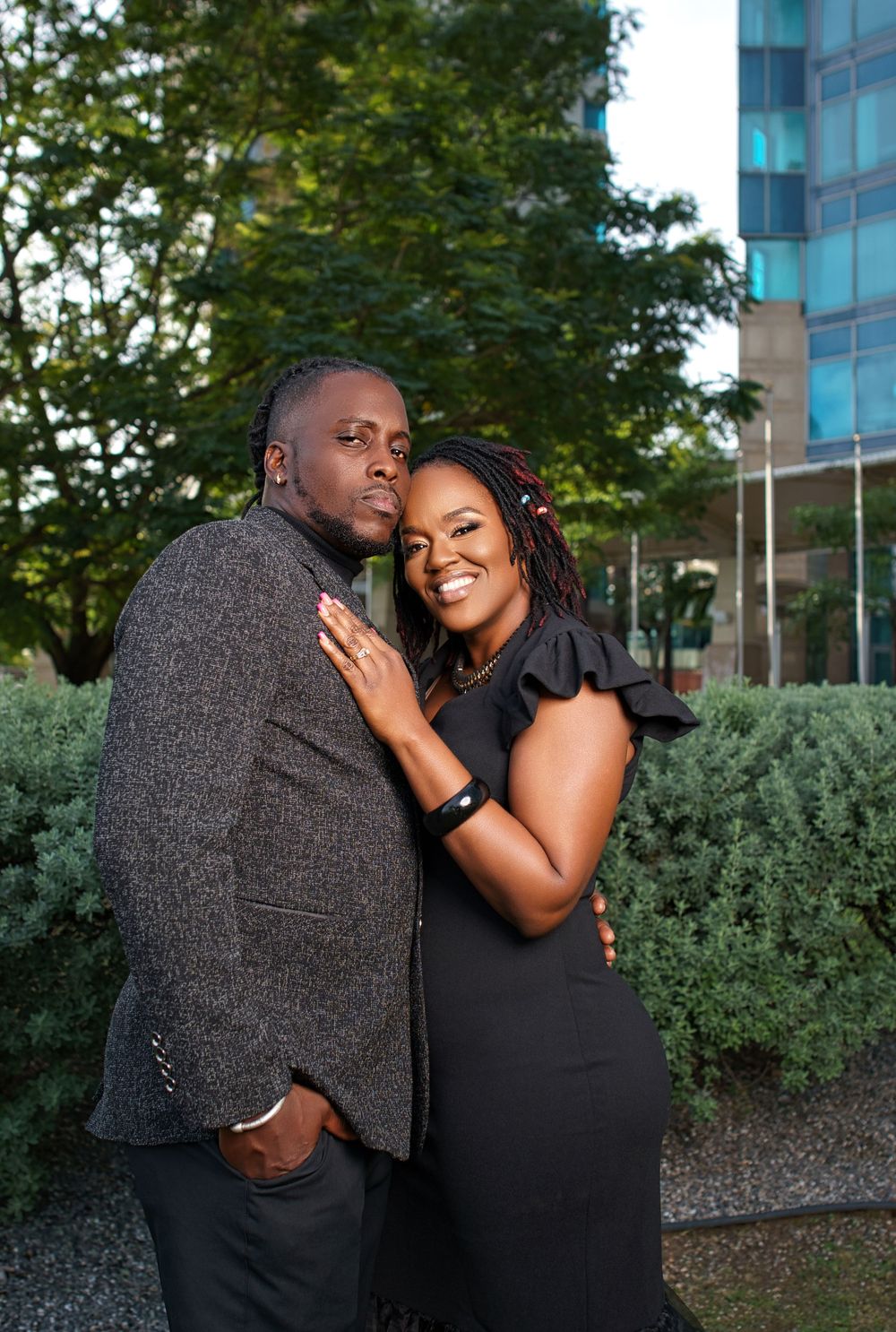 A romantic couple shares tender moments together in a garden setting with modern buildings in the background.