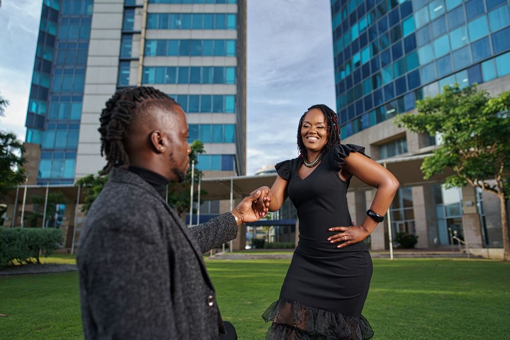 Two people share a joyful moment while conversing outside modern glass office buildings on a green lawn.