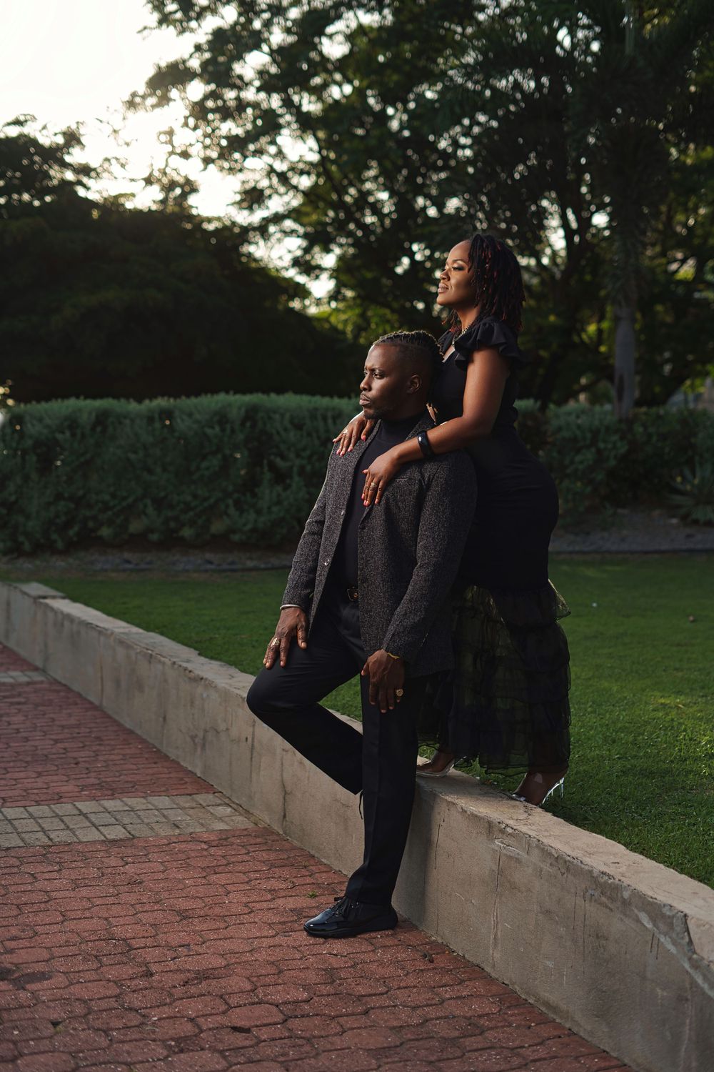 A couple shares an intimate moment on a brick wall during sunset in an urban garden setting.