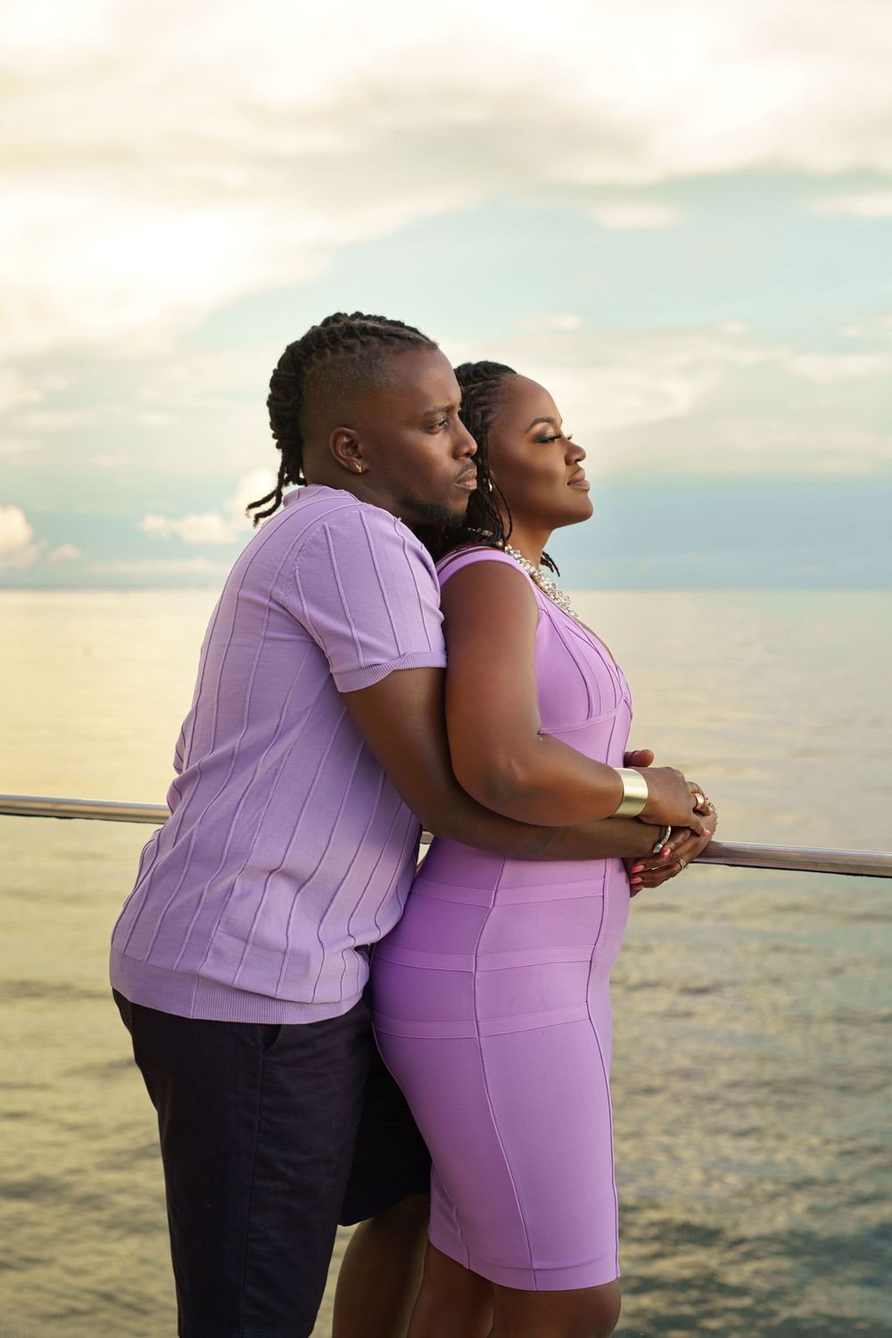 A couple in matching purple outfits embraces while looking at the ocean sunset.