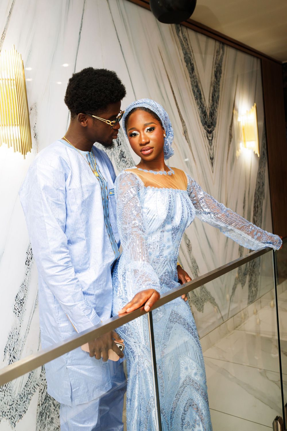A couple in matching light blue traditional attire pose together in an elegant setting with mirrored walls.