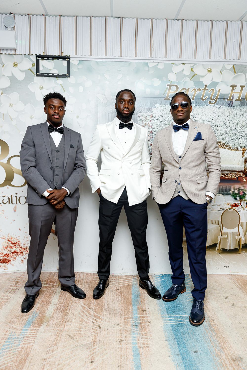 Three men in formal attire with bow ties pose against a decorated backdrop at an elegant event.
