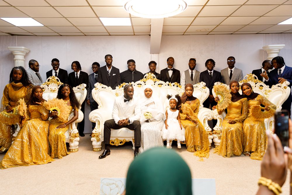 Large wedding party poses in elegant formal attire with bridesmaids wearing flowing gold dresses in church setting.