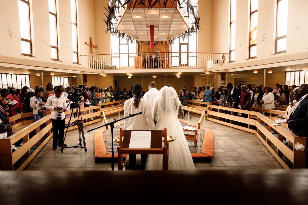Church congregation gathered in wooden pews during a worship service with natural light streaming through windows.