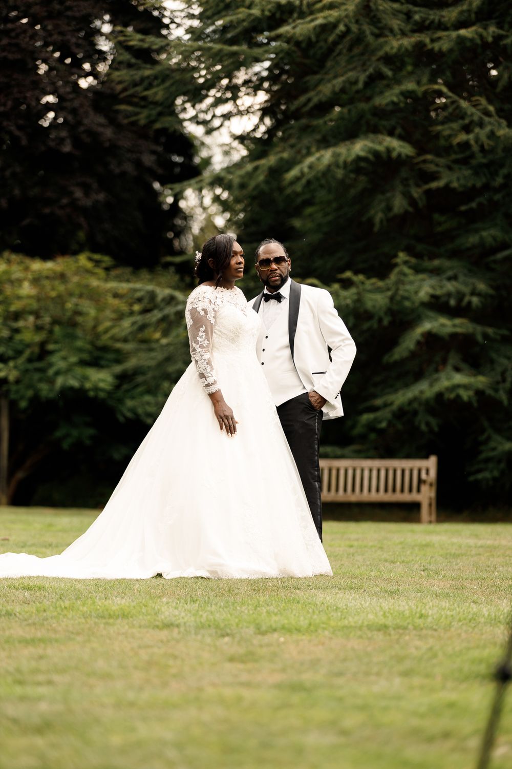 A romantic wedding couple shares intimate moments on a grassy lawn with evergreen trees in the background.