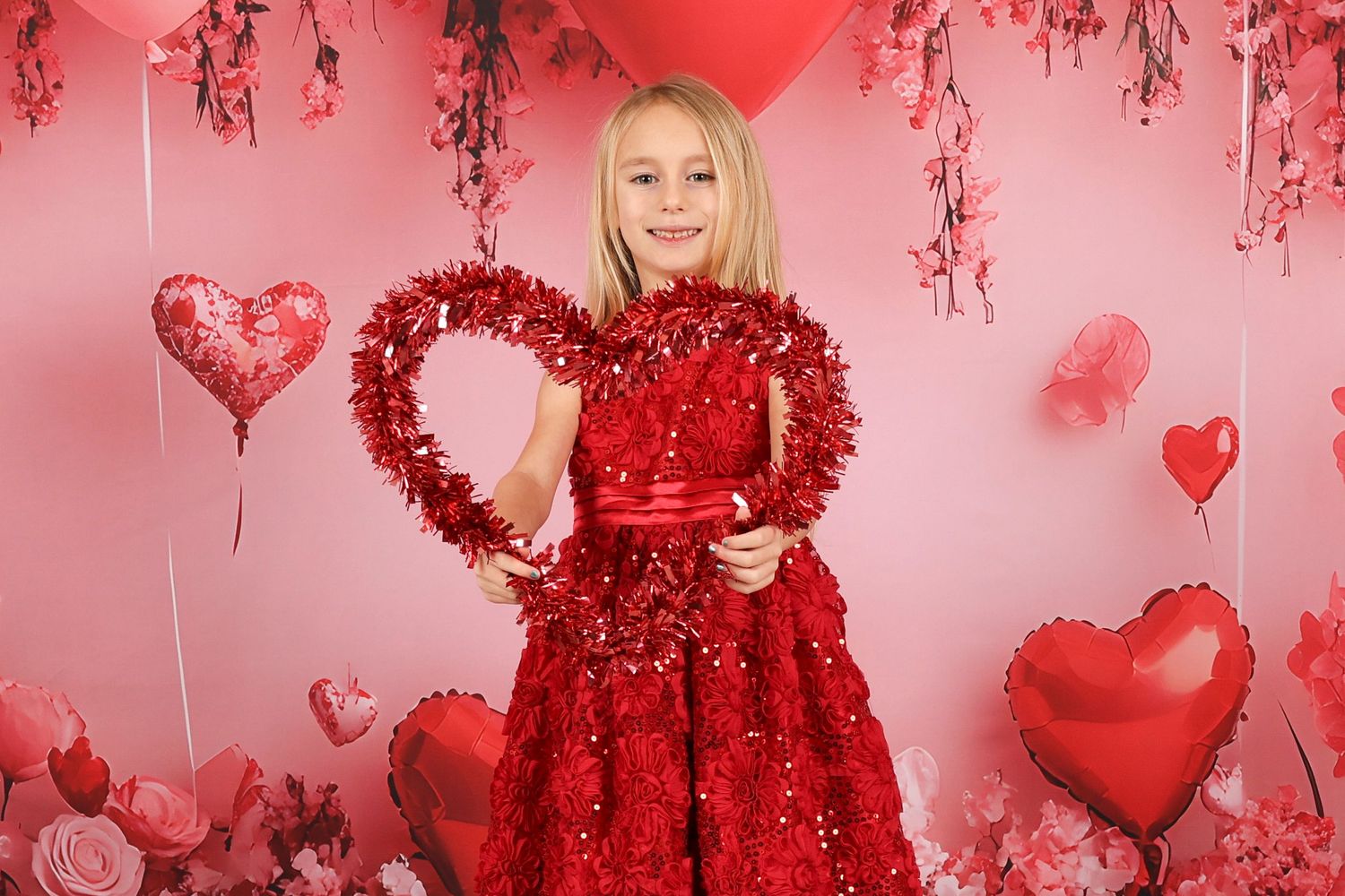 Valentine's portrait with large red heart decoration and sparkly dress against pink backdrop.
