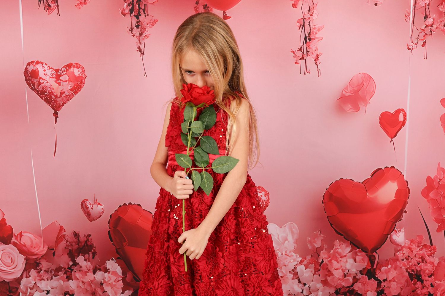 Red and pink Valentine's Day themed photo setup with heart balloons and romantic decor.