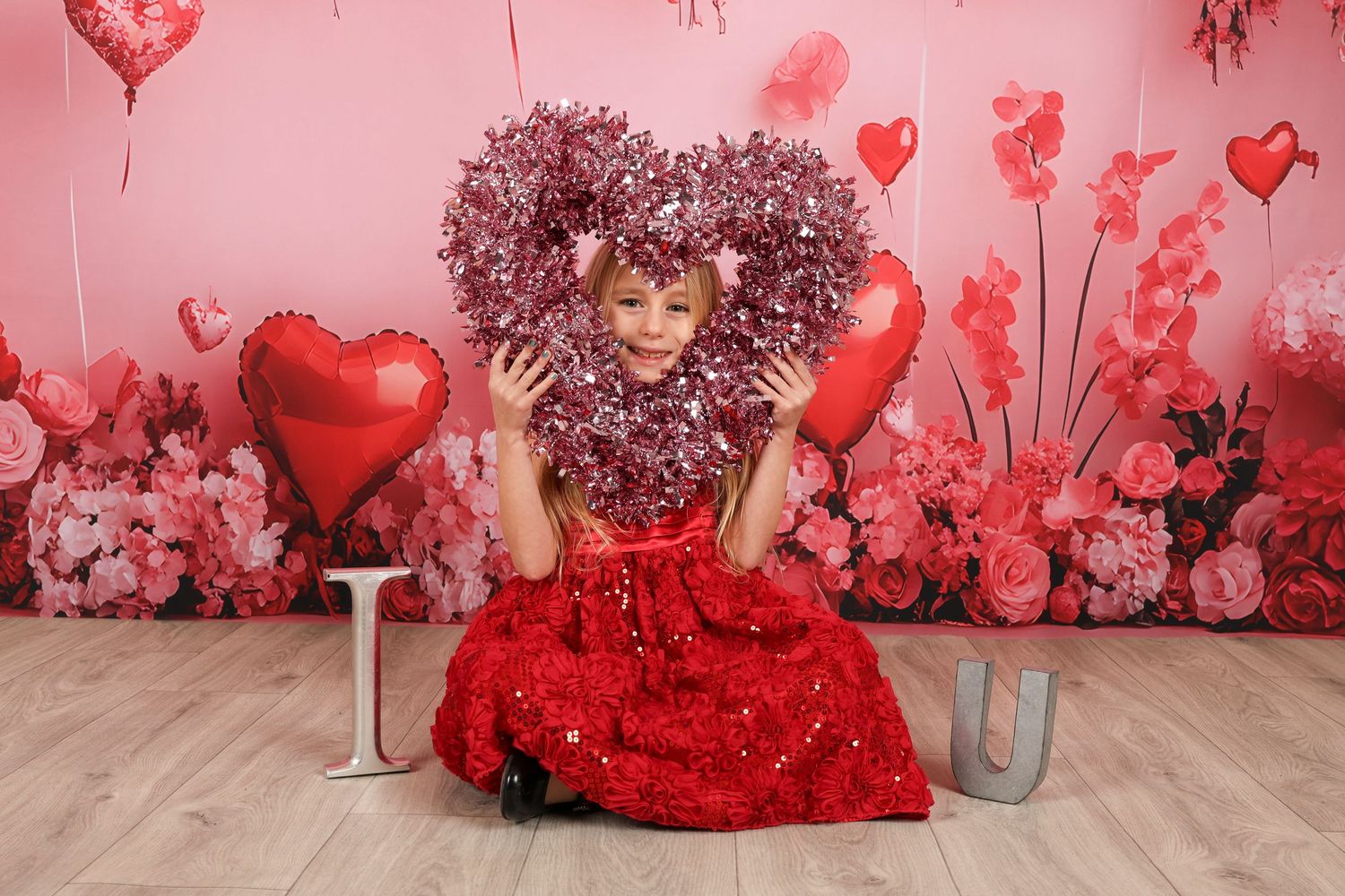 Valentine's portrait with large heart wreath and red sparkly dress against pink floral background.