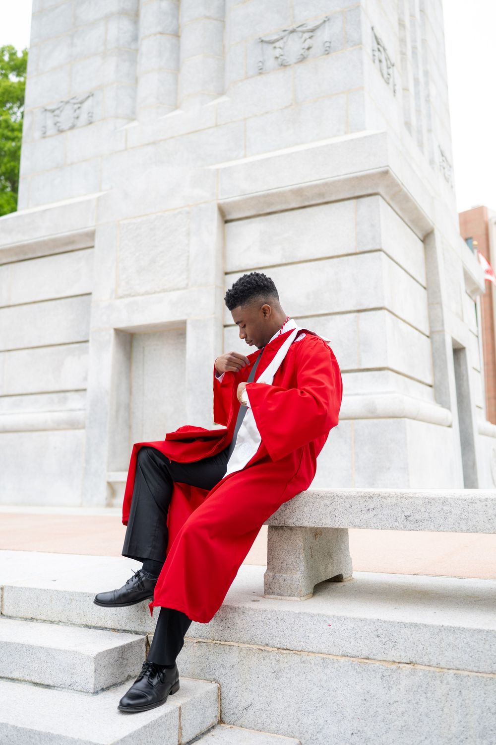 A person in a bright red blazer and black pants sits on white stone steps in a creative fashion photography pose.
