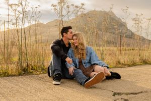 Couple sits together on path with mountain backdrop during golden hour.