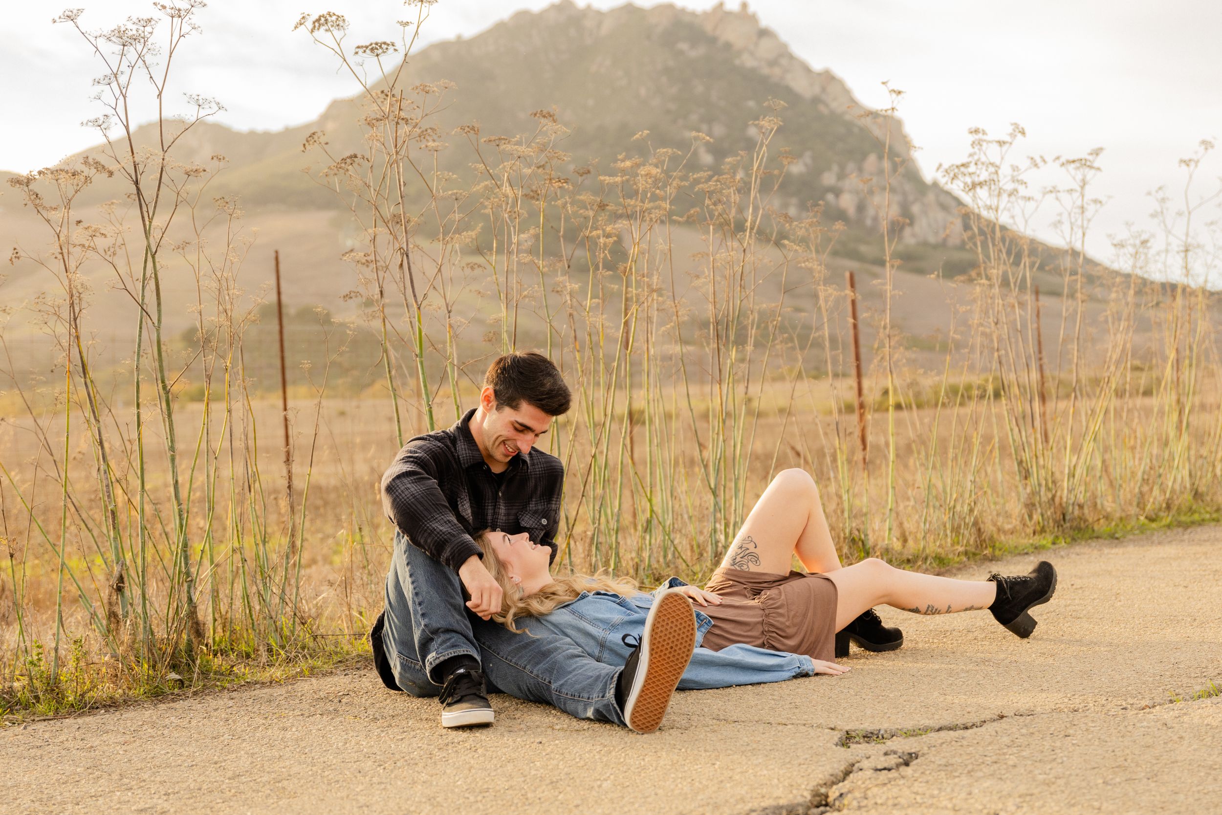Candid moment of couple relaxing on dirt path with mountain scenery.