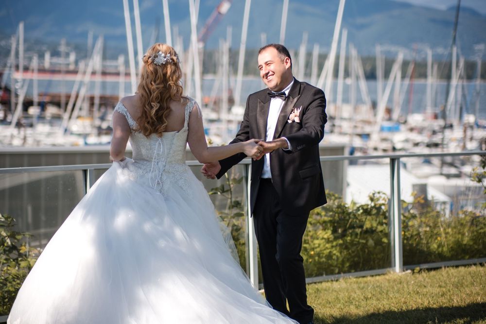 A couple in wedding attire shares a romantic moment together by a marina with boats and mountains in the background.