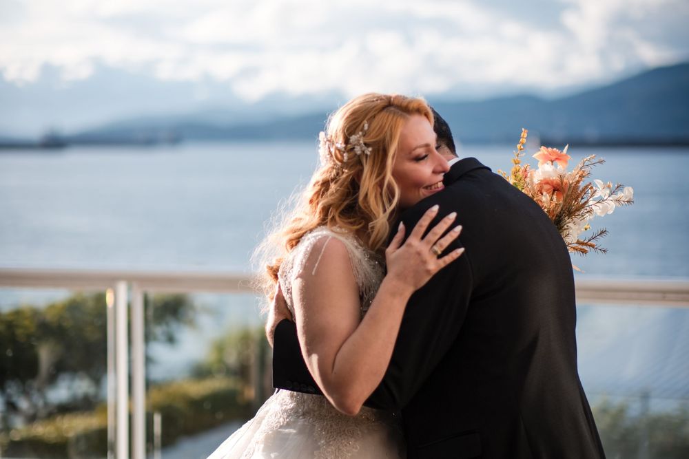A couple shares a romantic kiss during their wedding ceremony with mountains and water in the background.