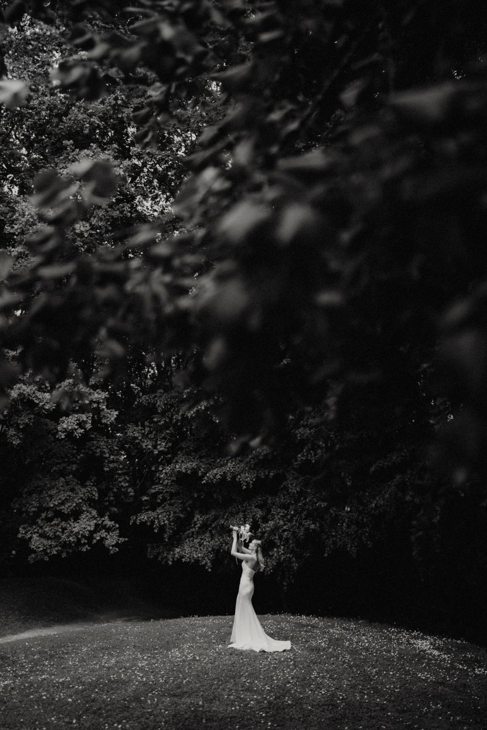 Dramatic black and white photo of couple standing in clearing surrounded by dark trees.