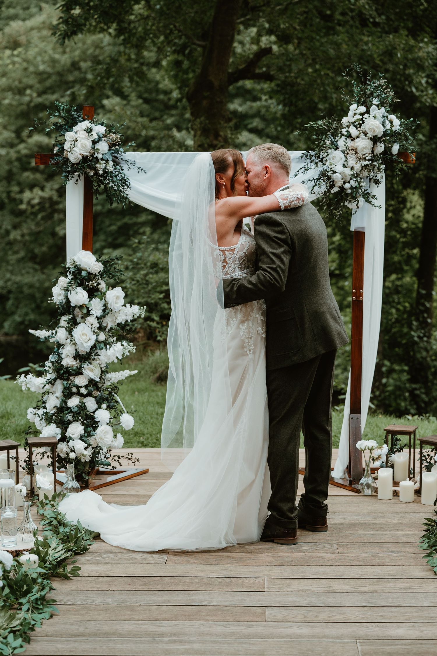 A romantic wedding couple shares a tender moment during their first dance under a white draped arch with floral decorations.
