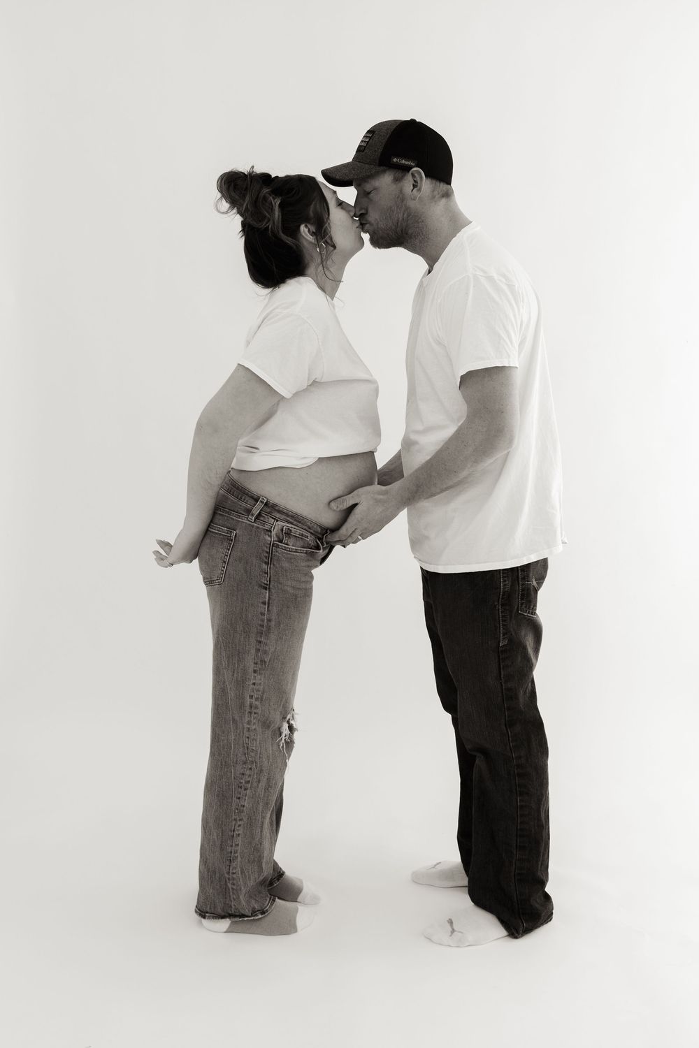Black and white portrait of expecting couple in denim and white shirts embracing.