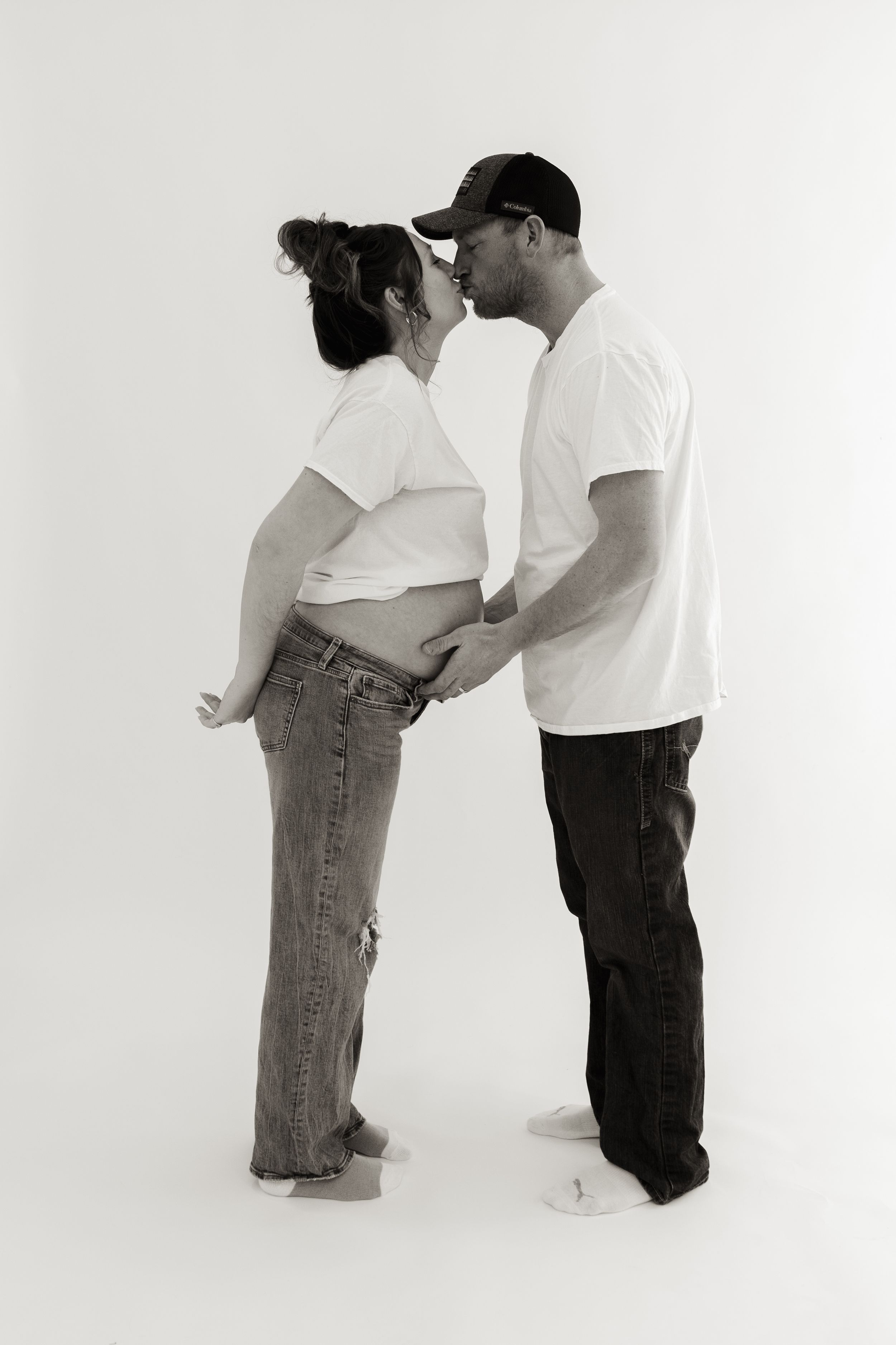 Black and white portrait of expecting couple in denim and white shirts embracing.