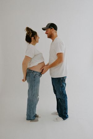 Couple in matching white t-shirts share intimate moment during maternity photoshoot.